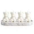 Four white teddy bear-shaped candles sitting on a white marble tray against a white background.