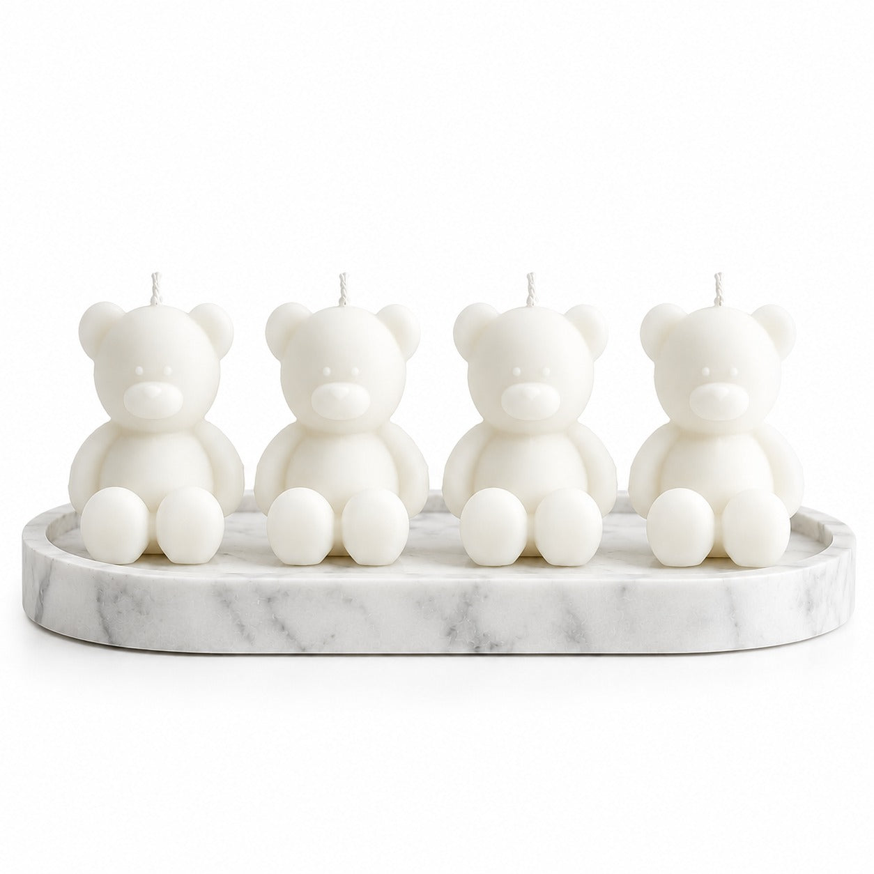 Four white teddy bear-shaped candles sitting on a white marble tray against a white background.