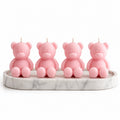 Four pink teddy bear candles arranged on a round white marble tray against a plain white background.