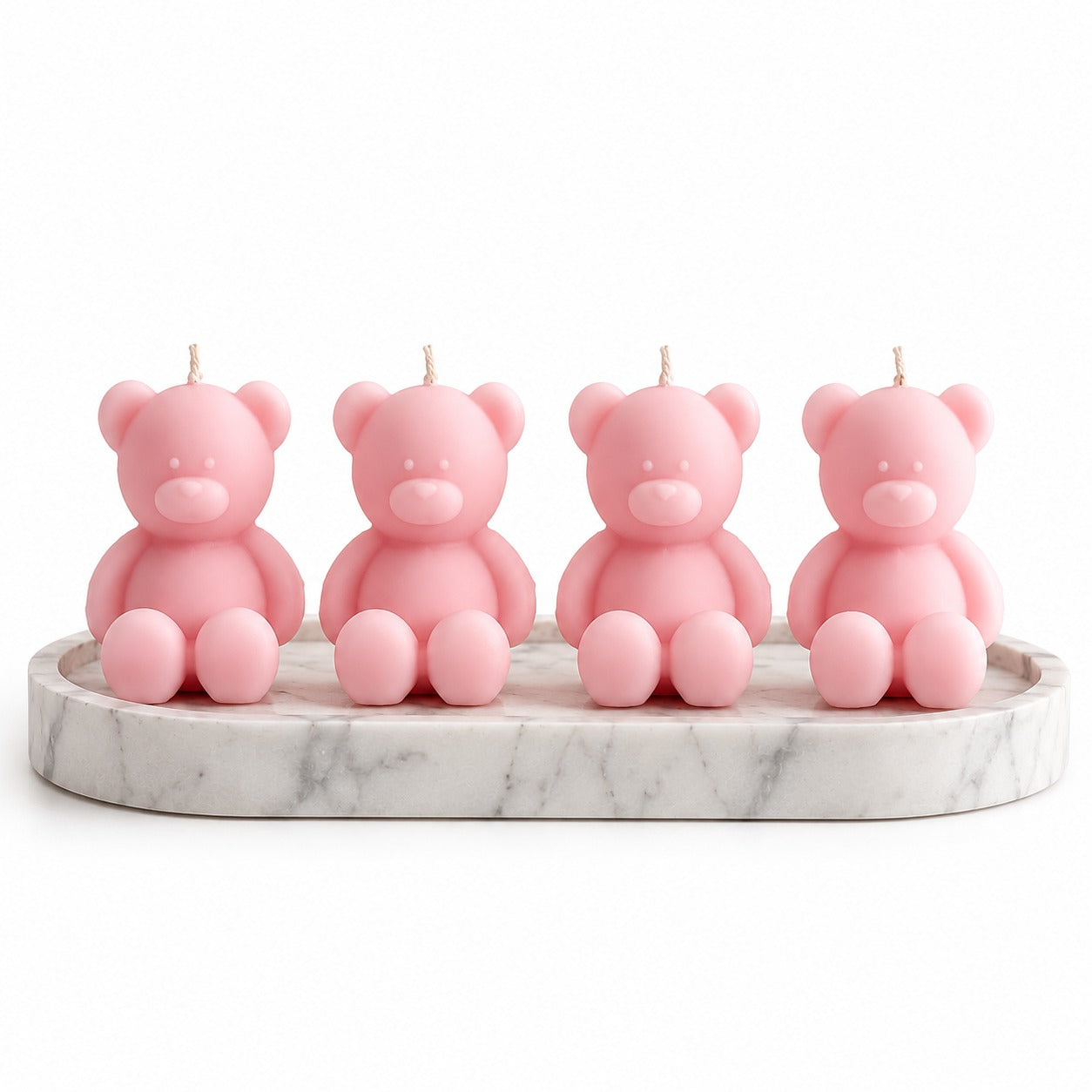 Four pink teddy bear candles arranged on a round white marble tray against a plain white background.