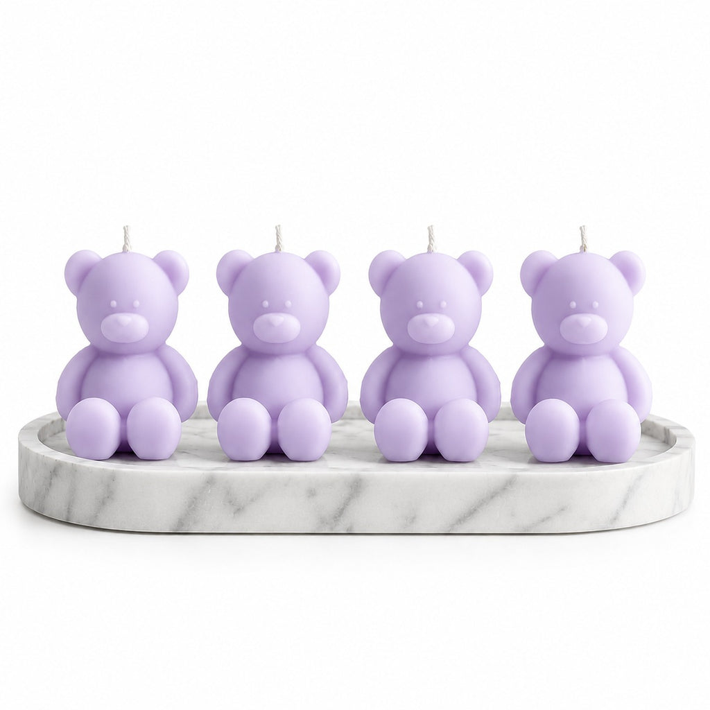Four lavender teddy bear candles arranged on a round white marble tray against a plain white background.