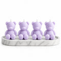 Four lavender teddy bear candles arranged on a round white marble tray against a plain white background.